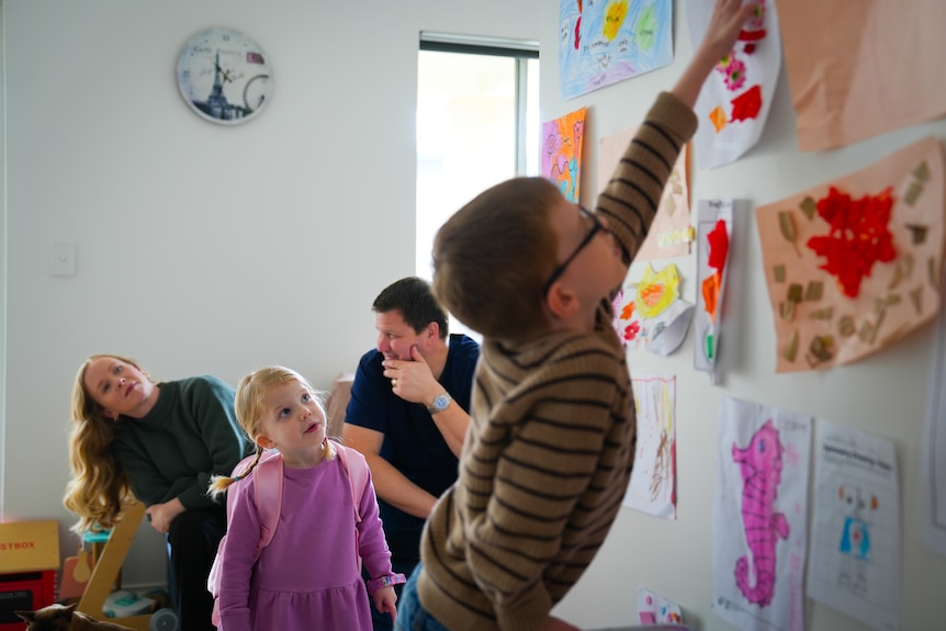 Patrick reaches up to a colorful picture on the wall with his parents behind him.