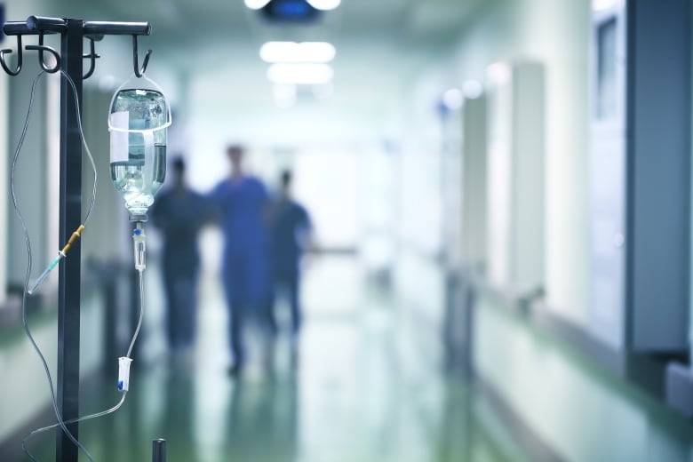 An IV unit is shown in the foreground in a hospital corridor. 