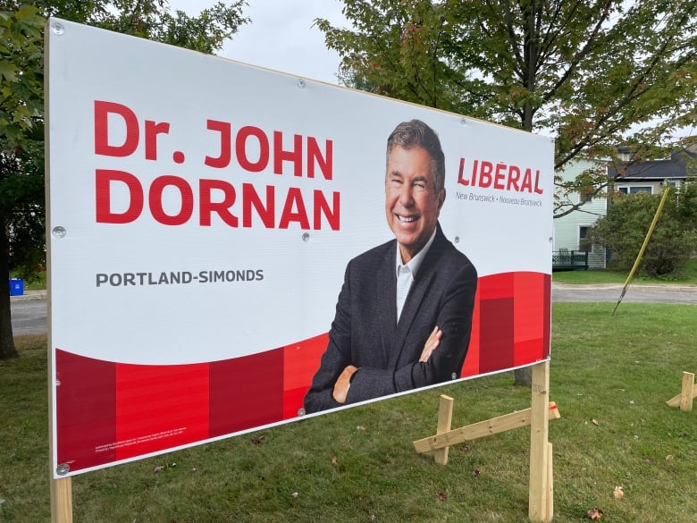 A large billboard stands on a grassy lawn with a picture of a smiling man on it.