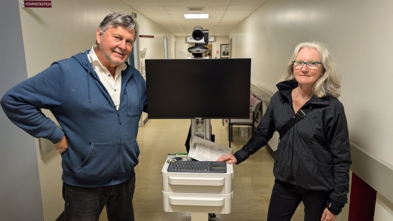 Two men stand with a telemedicine unit, which is a TV screen with a camera and a laptop 