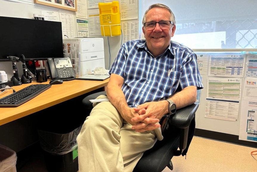 A doctor sits in a chair in a clinic and smiles for the camera