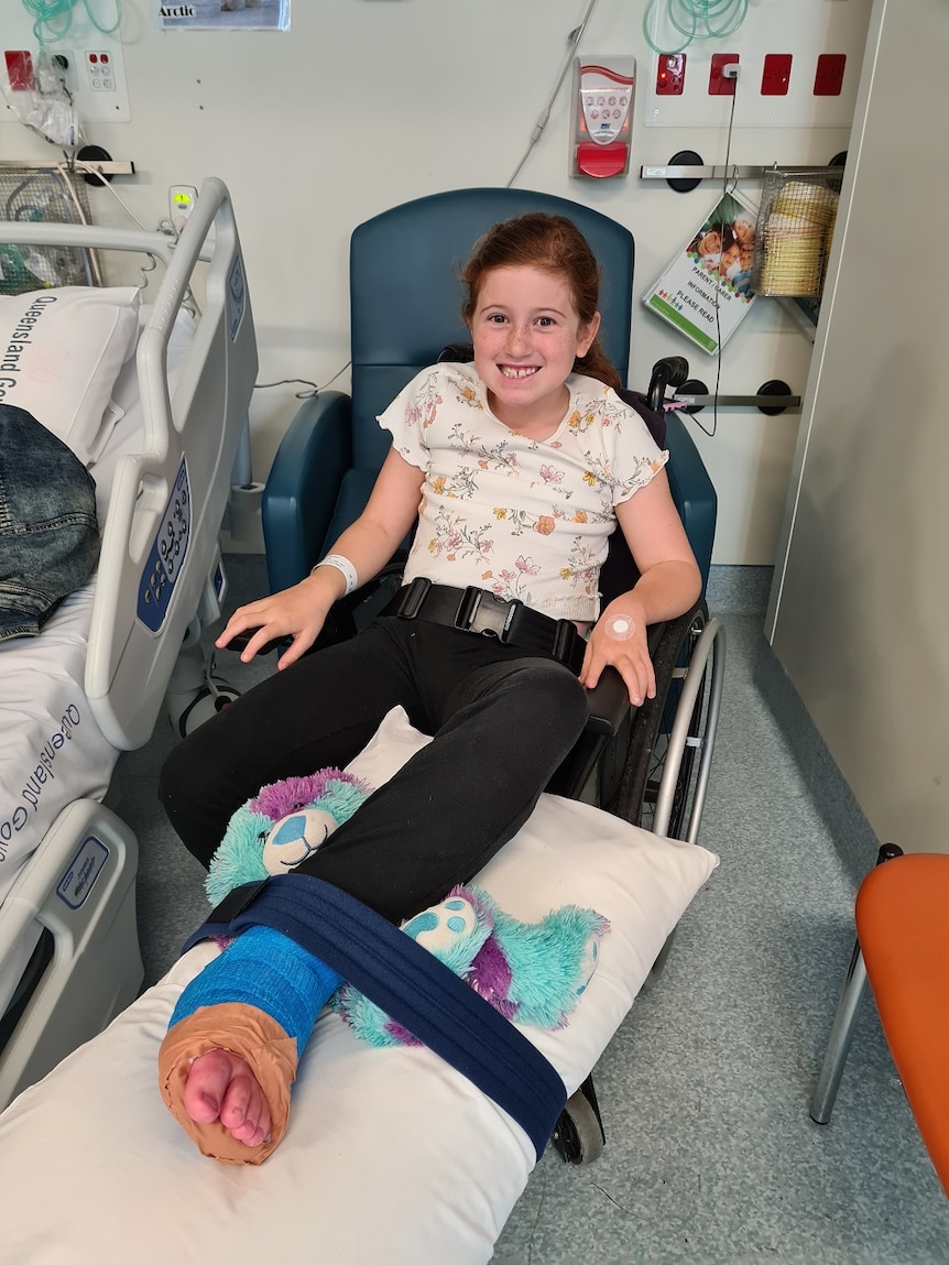 A girl sits in a wheelchair with a cast on her leg