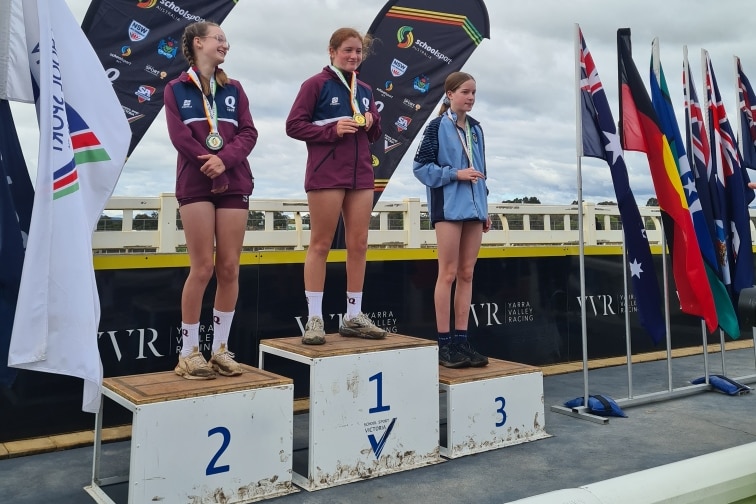 Three girls stand on a platform with medals around their necks