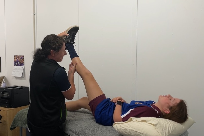 A woman does leg exercises with a girl lying on a massage table