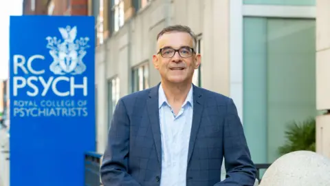 Grainge Photography Dr Ulrich Müller-Sedgwick stands in front of the office of the Royal College of Psychiatrists.