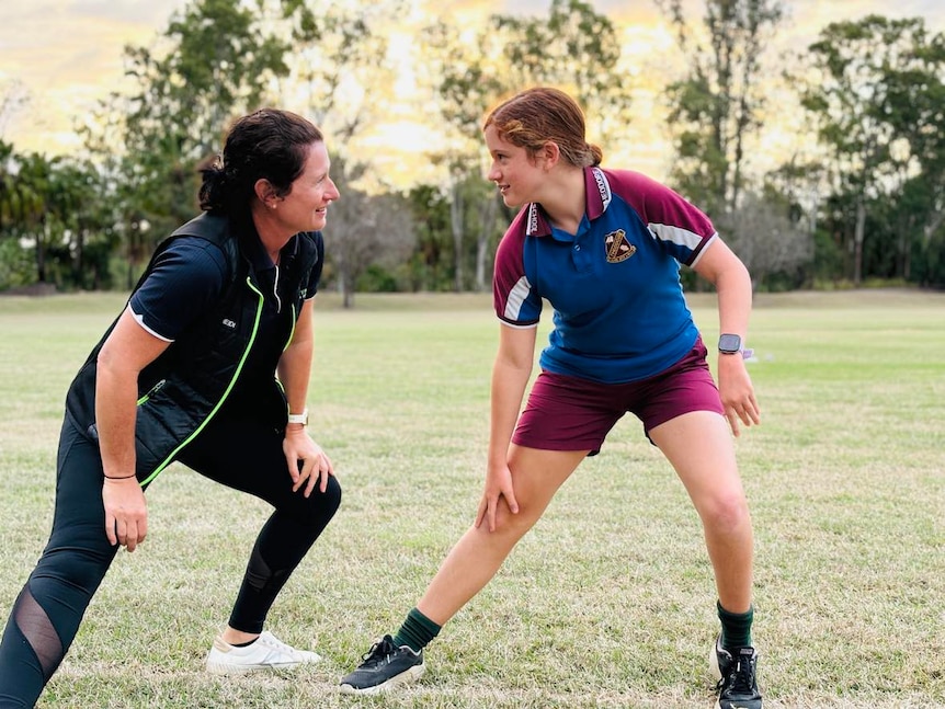 A woman and a girl stretch out on a patch of grass while looking at each other